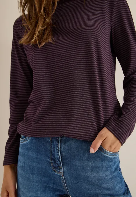 Frau mit lila gestreiftem Pullover und blauer Jeans, Hand in der Hosentasche.